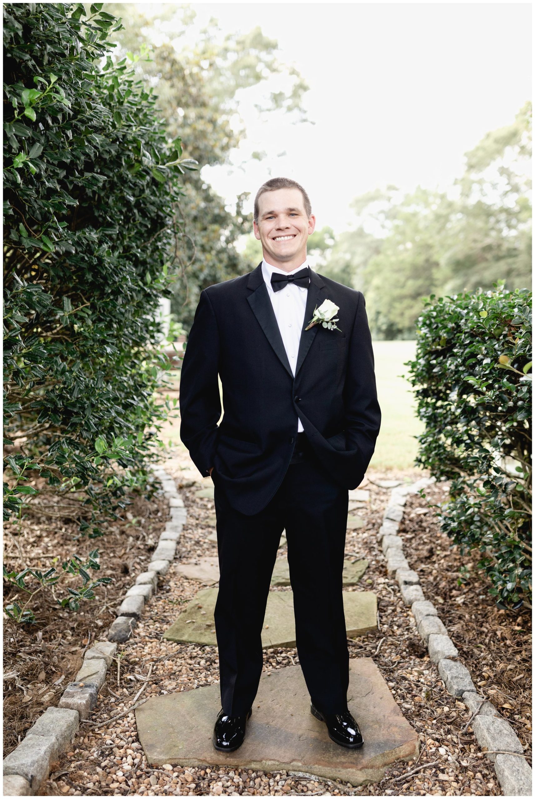 groom standing on path with greenery,