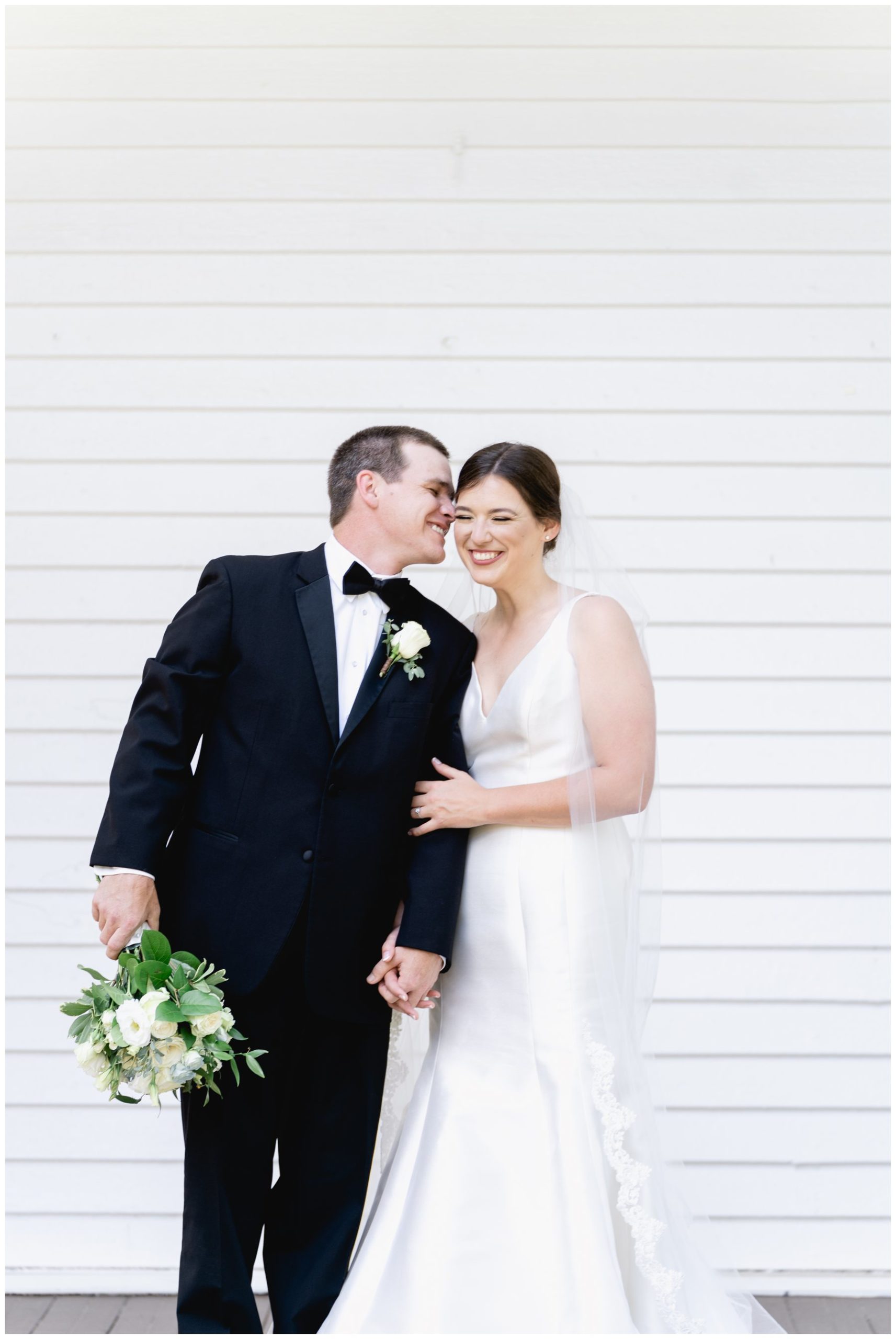 groom touching nose to bride's temple while holding her bouquet,