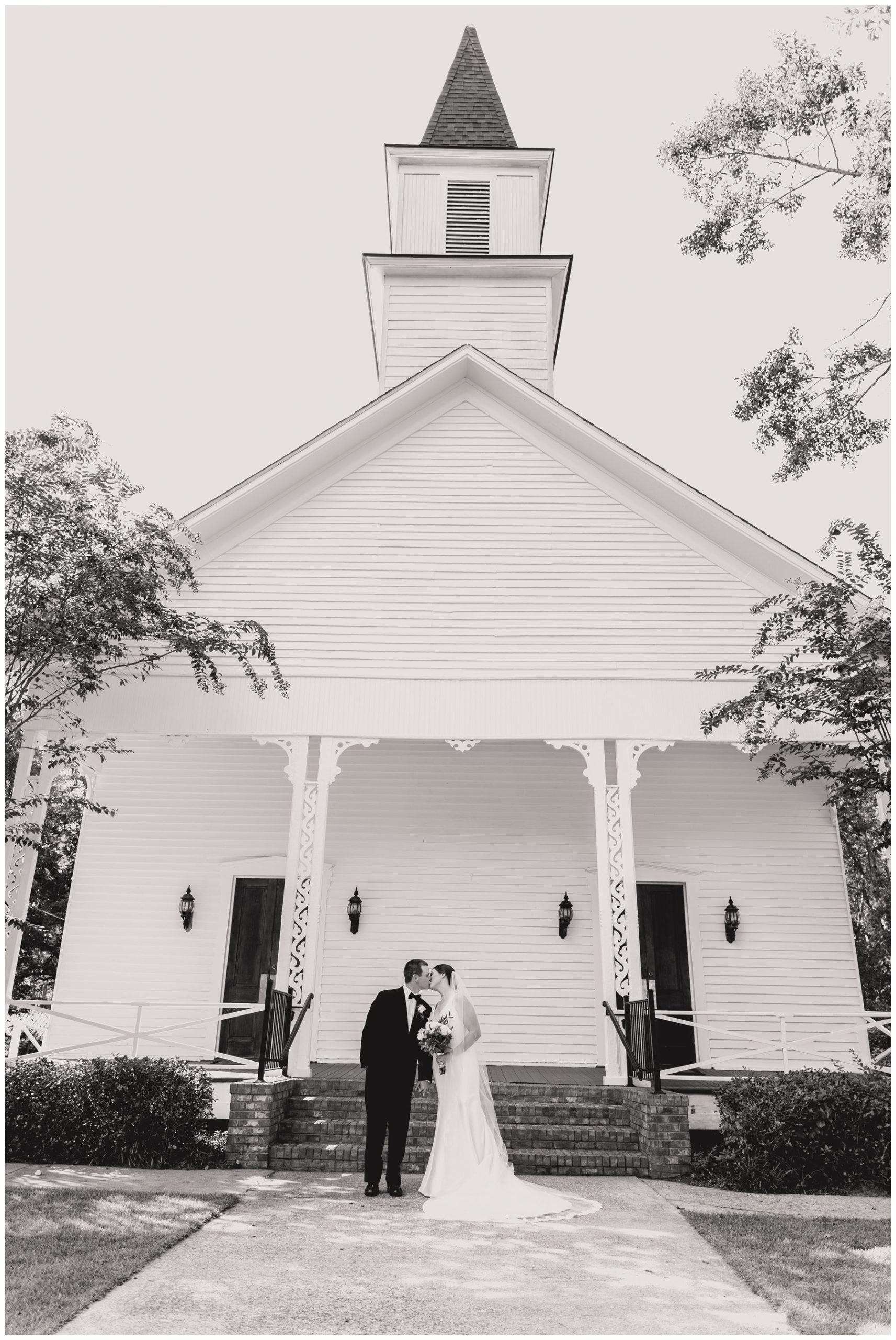 black and white of bride and groom kissing in front of Lowndesboro Baptist Church,