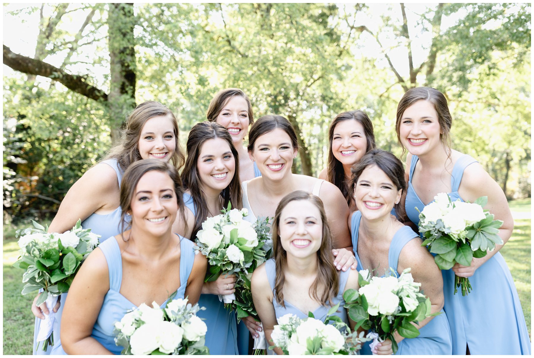 bridesmaids wearing blue dresses holding white rose bouquets in a clump,