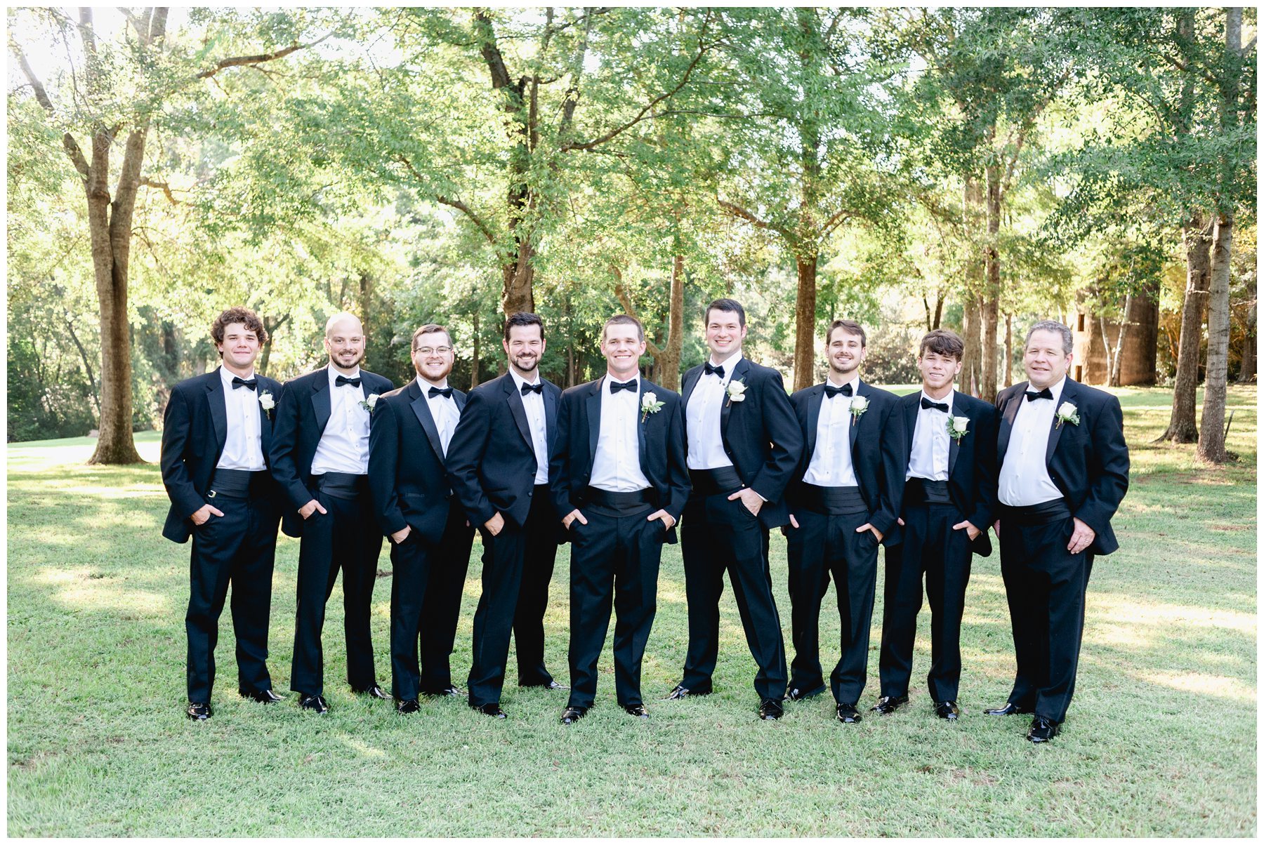 groomsmen standing in a line wearing black with white boutonnieres,