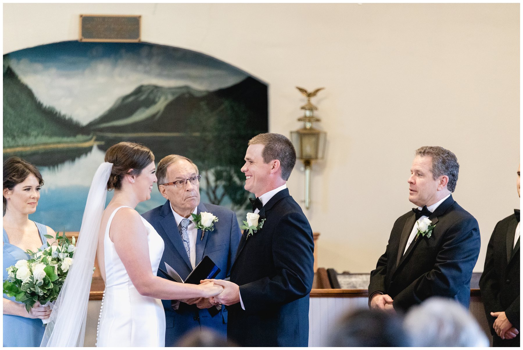 groom and bride smiling at each other in front of preacher at altar,