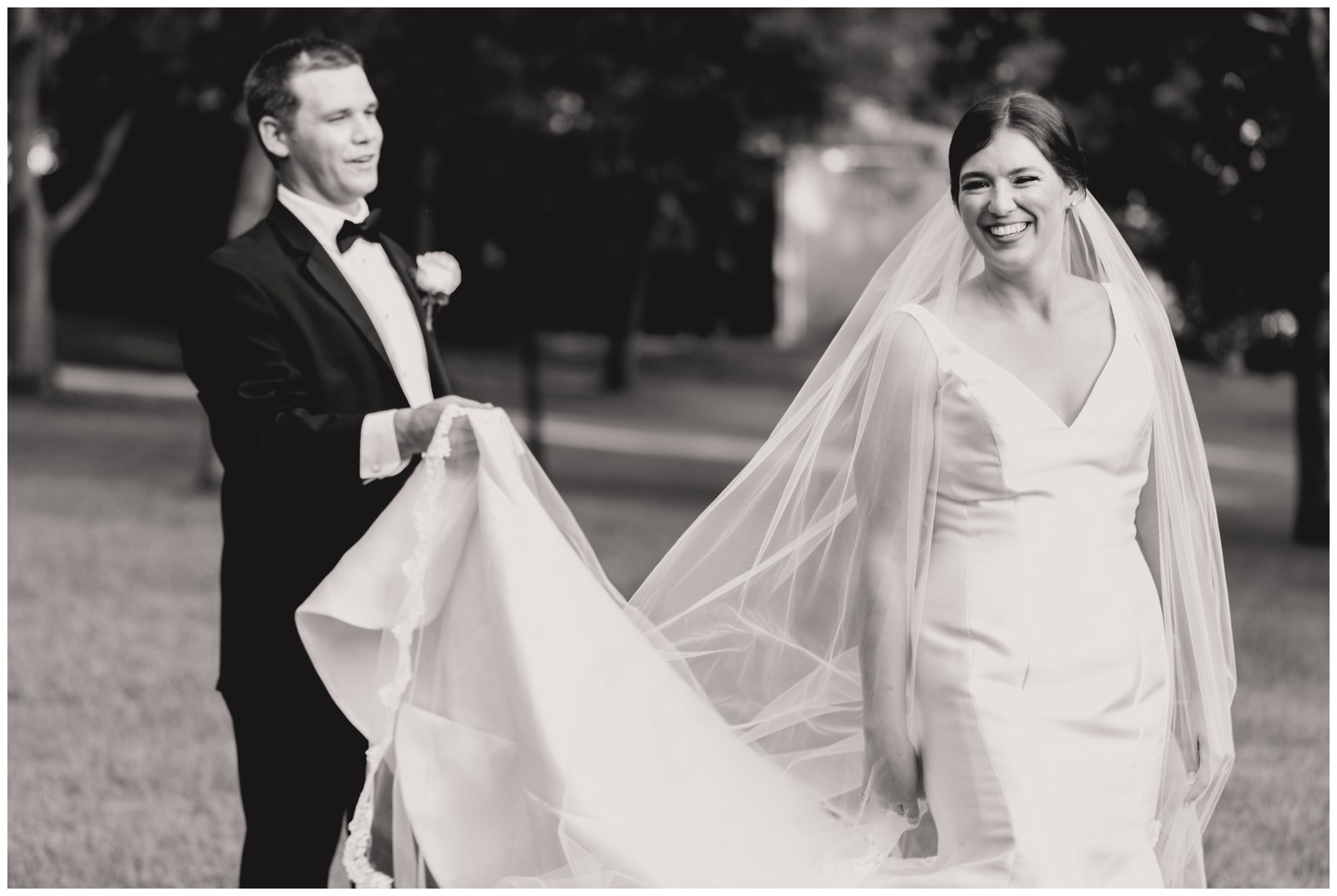 black and white of groom helping carry smiling bride's dress,