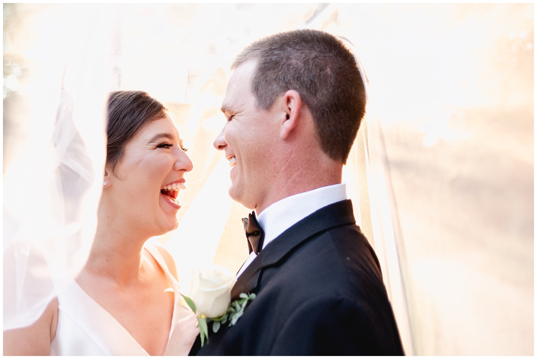 vibrant color image of bride and groom laughing under her veil with sunset in background,