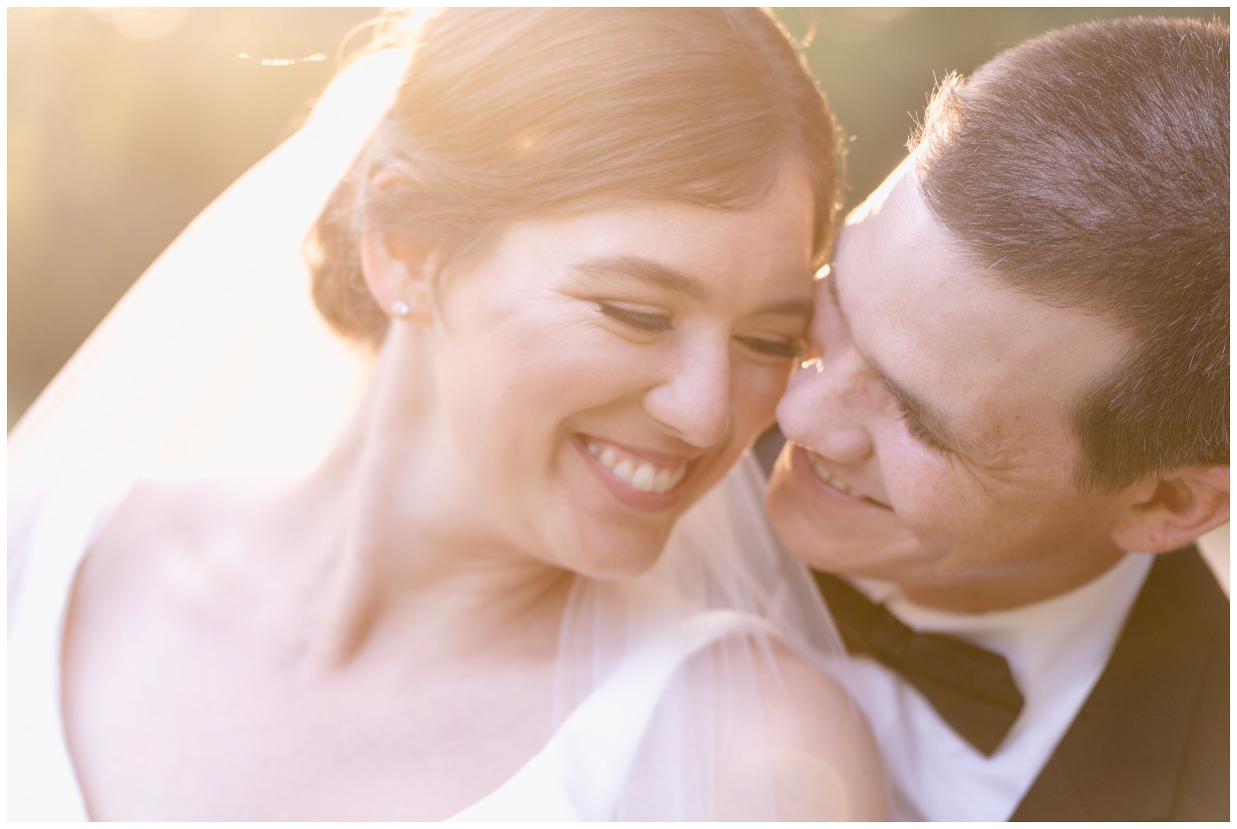 groom nuzzling bride from behind with sunset in background,