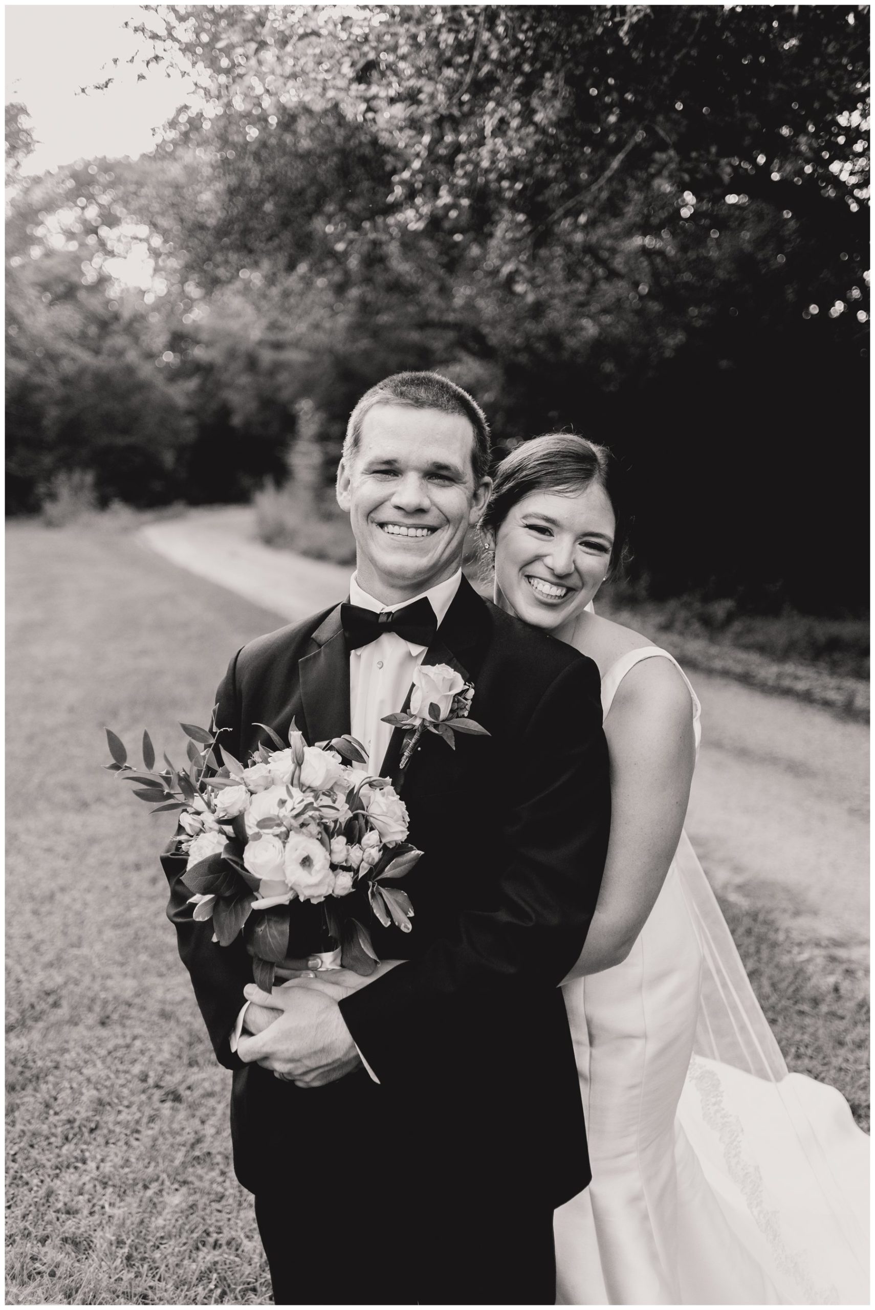 black and white of bride hugging groom from behind and both smiling,