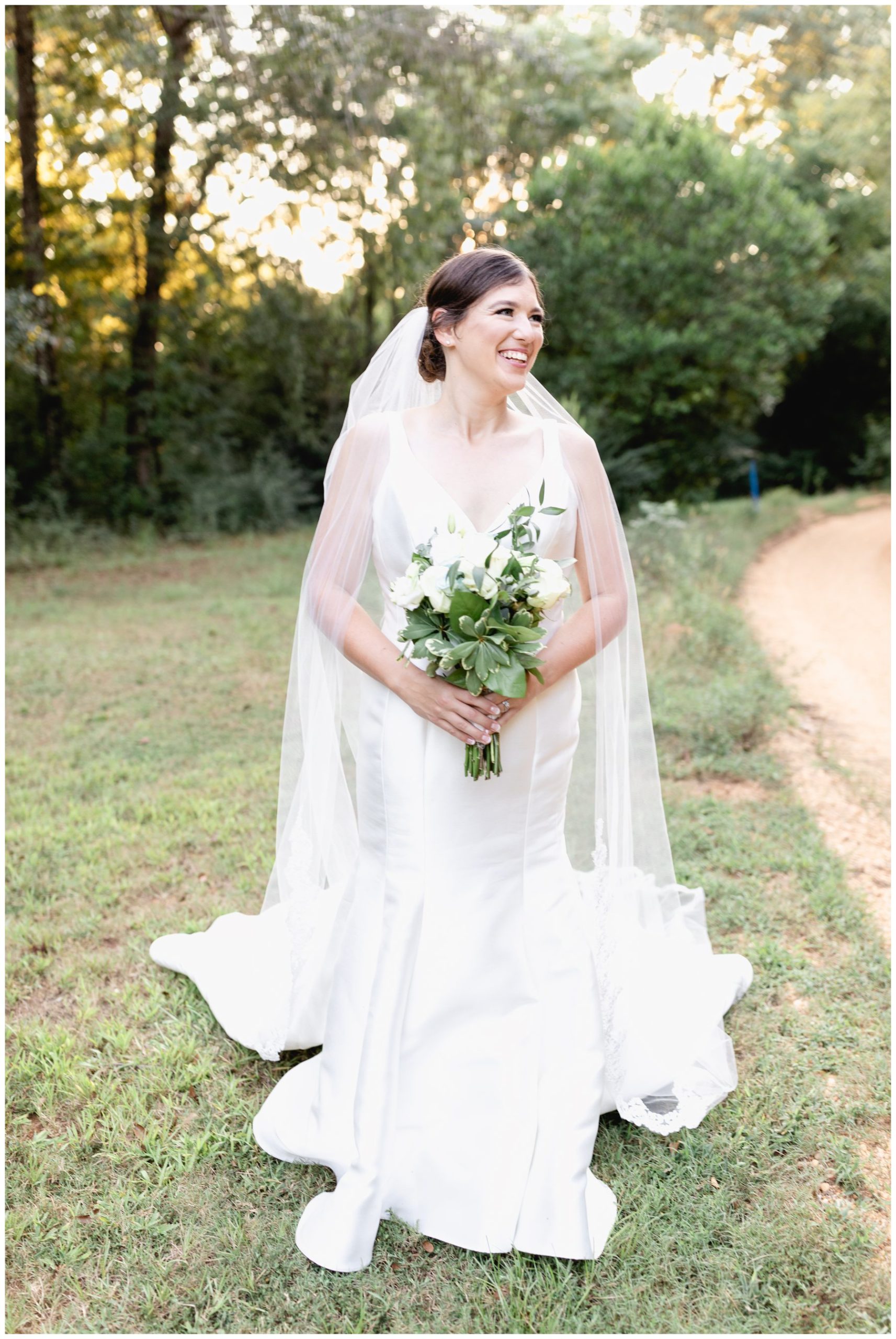 bride smiling to the right with sunet in background while holding white flowers,